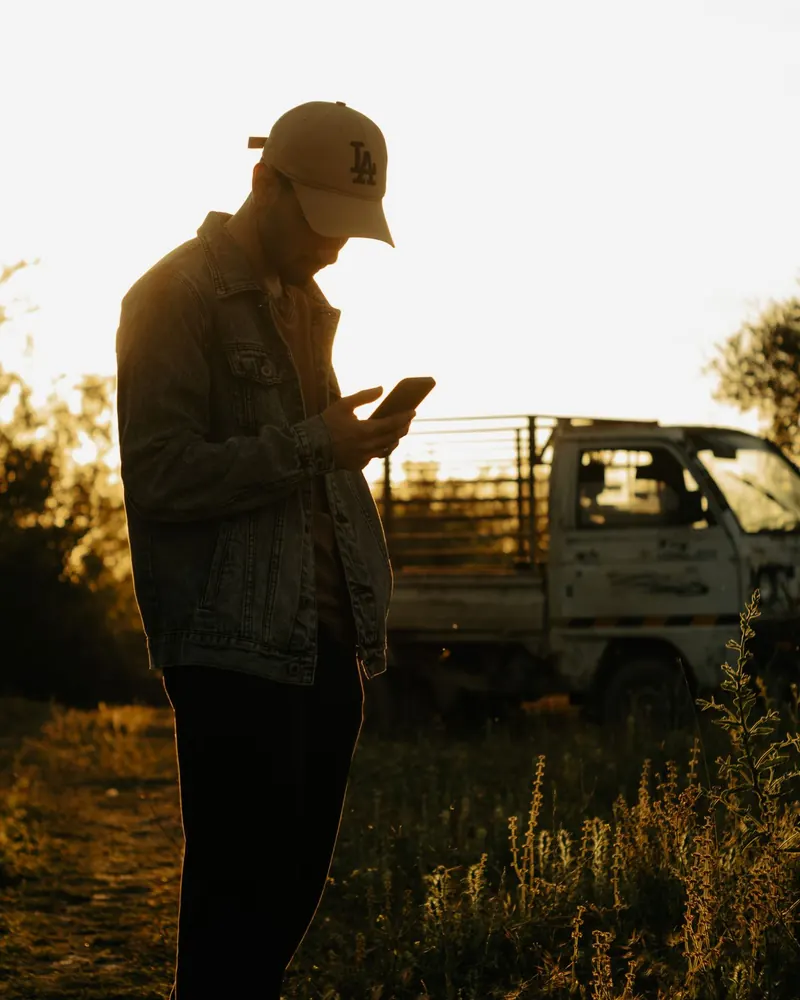 A man checking his phone beside a truck at sunset